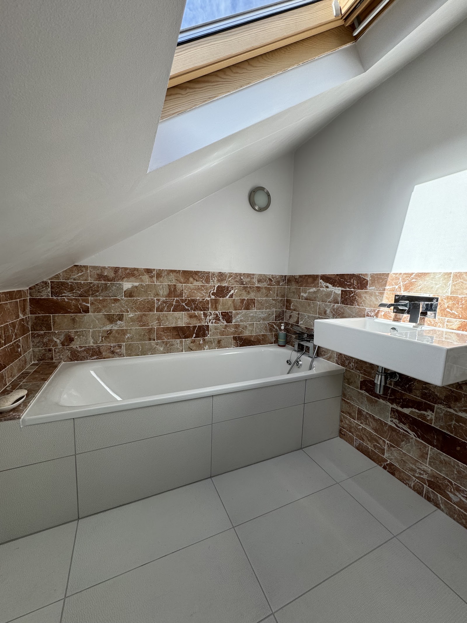 A loft bathroom under the eaves — bath, basin and marble-effect tiling.