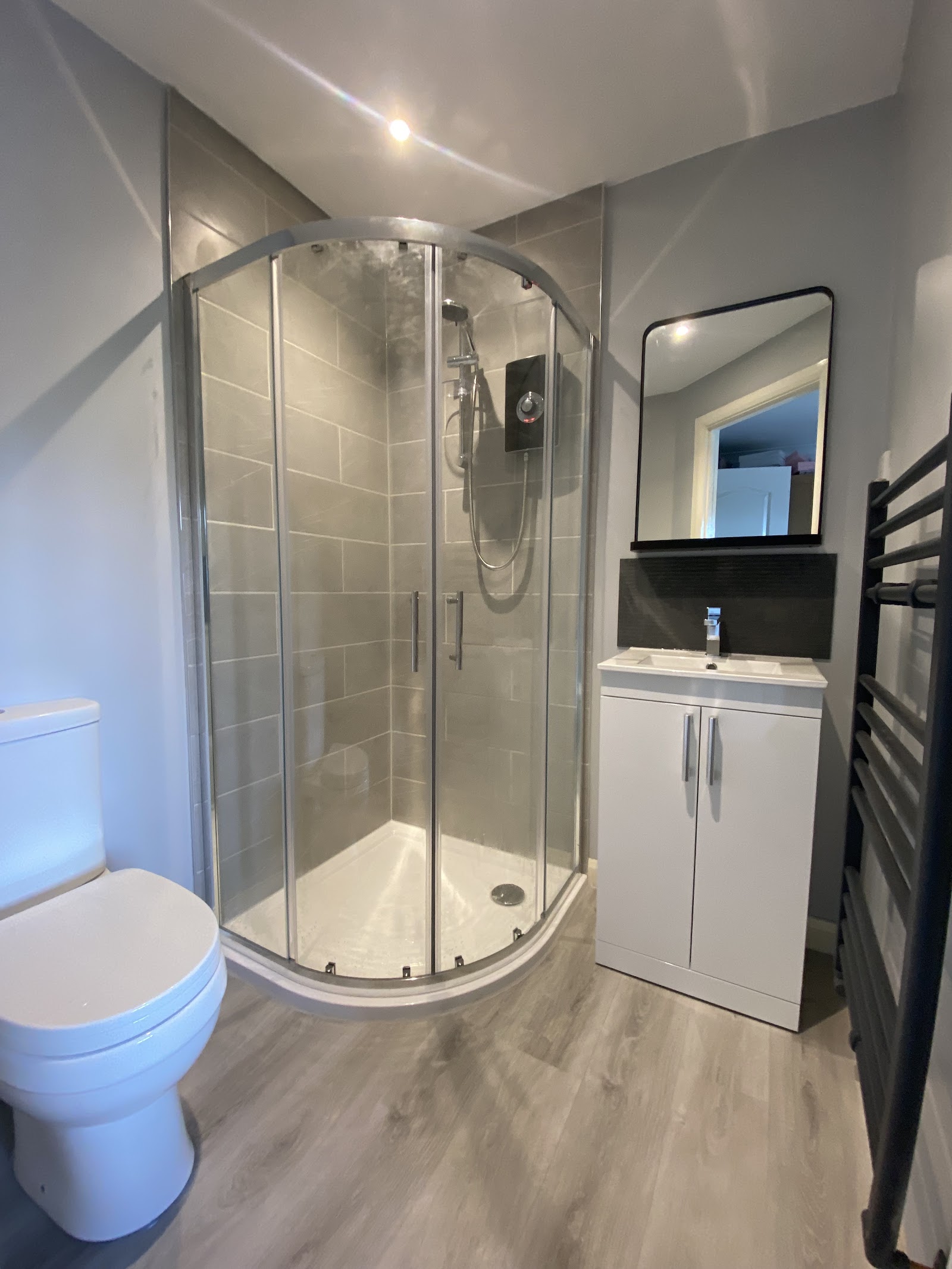 Compact en suite with a quadrant shower, vanity unit and towel radiator.