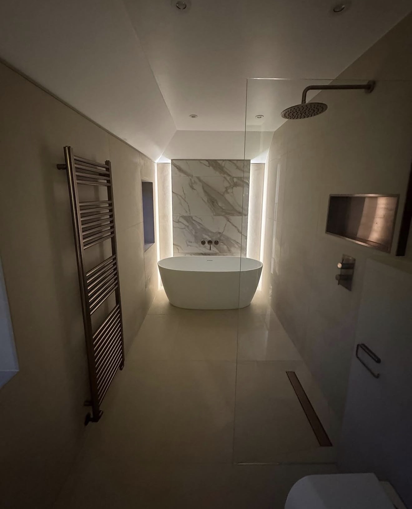A backlit marble feature wall and freestanding bath, lit for the evening.